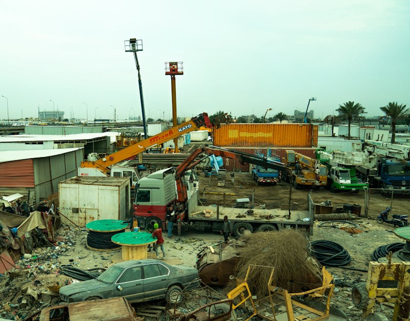An industrial scrap yard featuring cranes, trucks, and scattered debris.