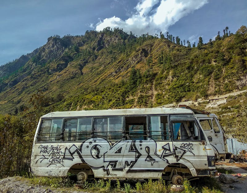 An abandoned graffiti-covered bus set against a scenic mountainous landscape under blue skies.