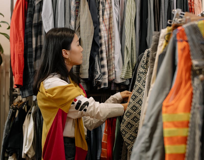 A young woman browsing clothes in a vintage store with colorful outfits.